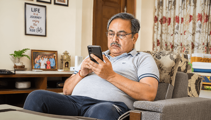 A old man with obesity sitting on a sofa and using a smartphone