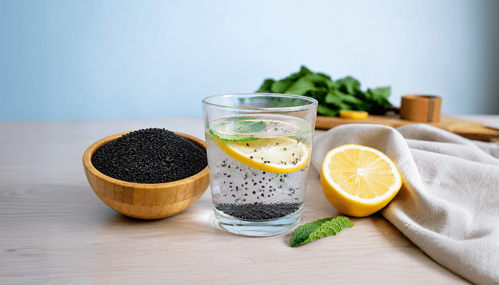 kalonji water drink with lemon beside a bowl full of black kalonji seeds