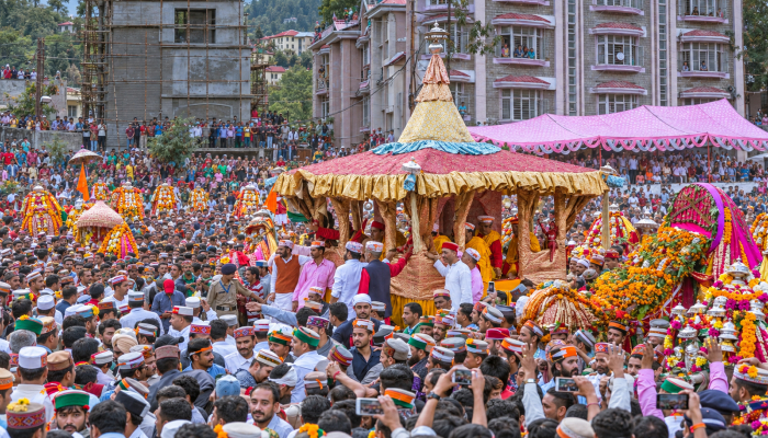 an image showing the still of kullu Dussehra celebration where people gather to lift over 200 local deities in decorated palanquins which are then carried to Dhalpur Maidan to honour Lord Raghunath.