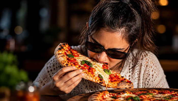 a girl devouring pizza as she experiences the hunger hormone ghrelin due to an energy crash and lack of satiety.