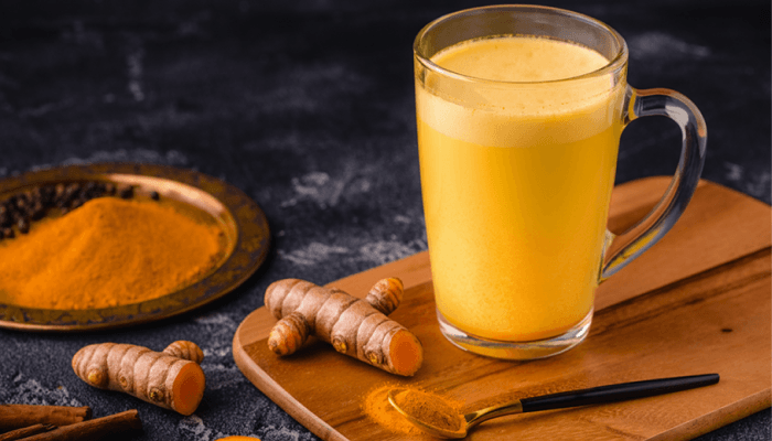 haldi doodh in a glass with raw turmeric